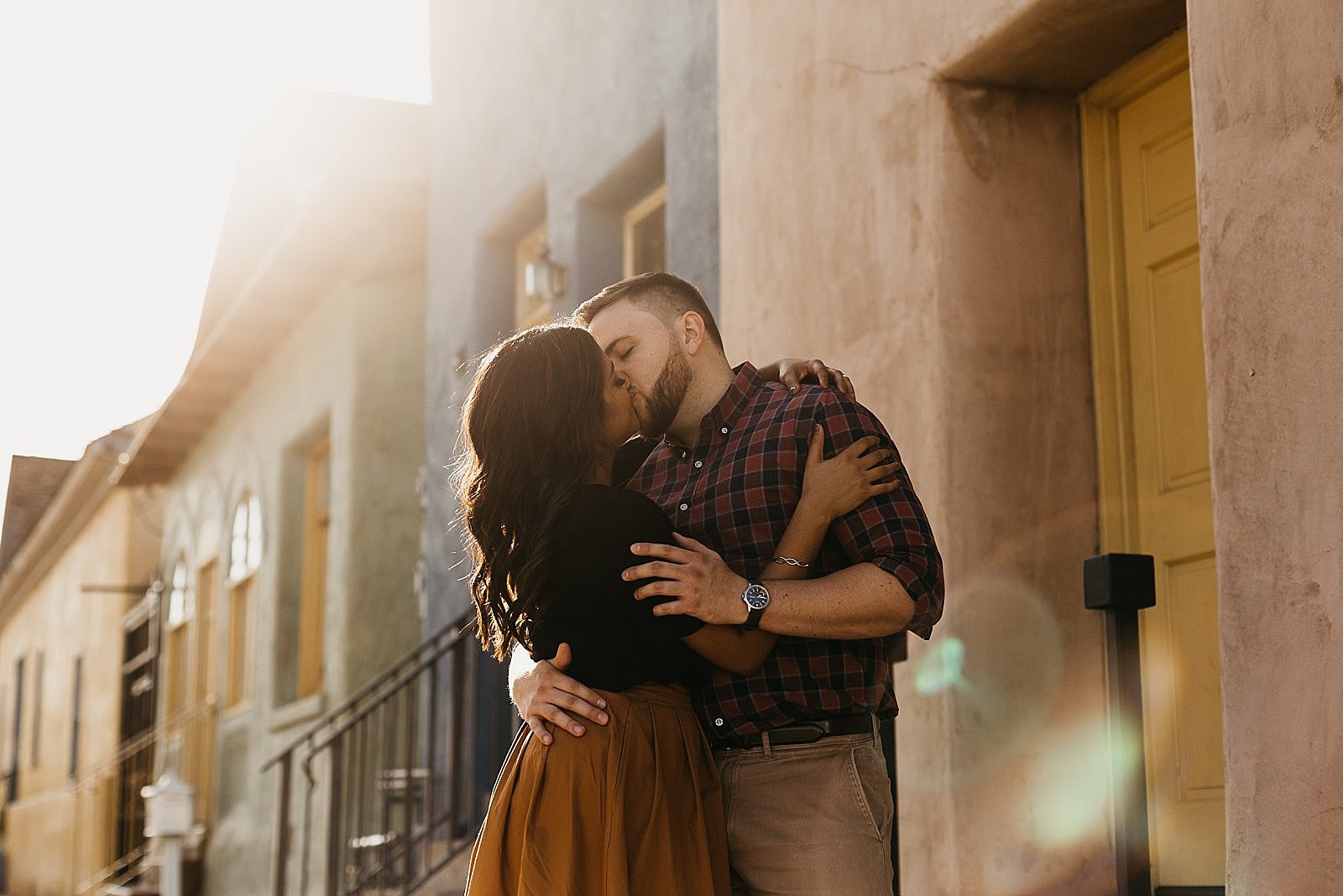 couple kissing in the street by colorful adobe houses in tucson az for their engagement photos by samantha patri