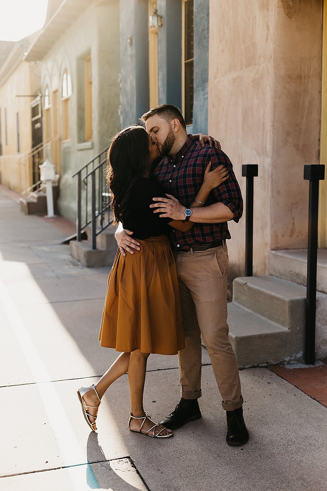 couple kissing in the street by colorful adobe houses in tucson az for their engagement photos by samantha patri