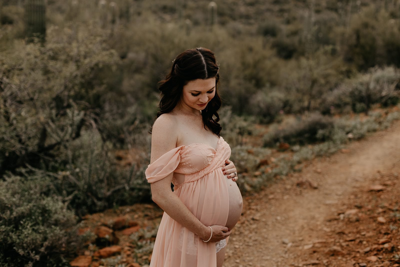 Mum in pink dress looking down at her belly maternity photos in phoenix AZ