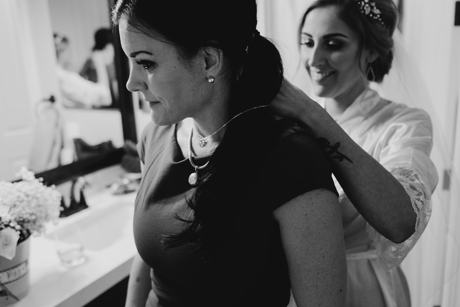 Bride putting on her mother-in-law's necklace in black and white