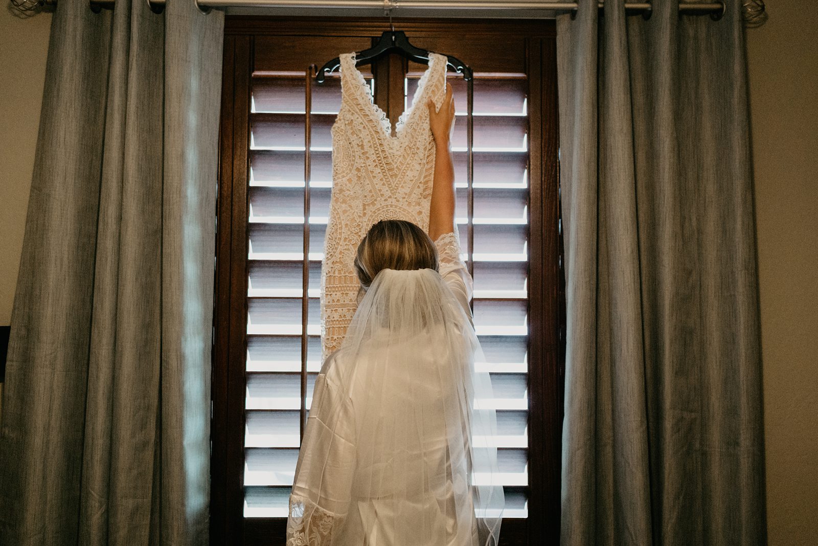 Bride reaching for her dress that is hanging up on a window