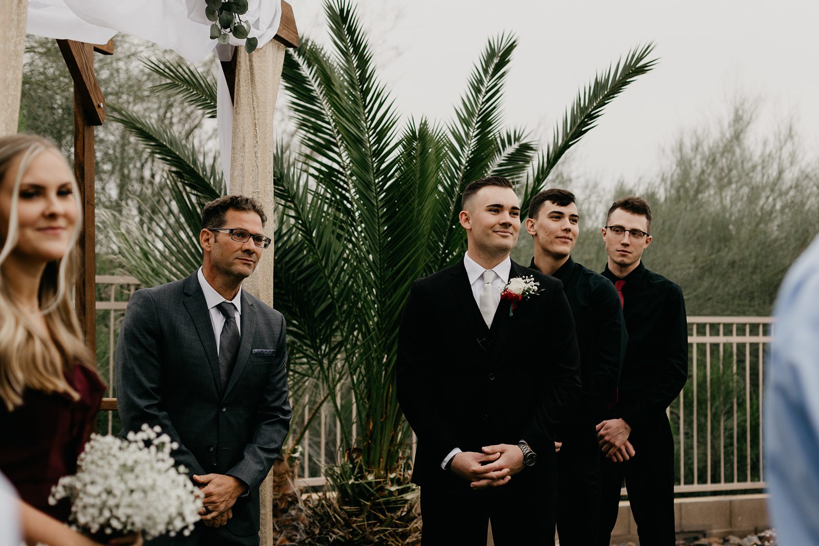 A groom smiling watching his bride walk down the aisle for his backyard elopement in Glendale AZ