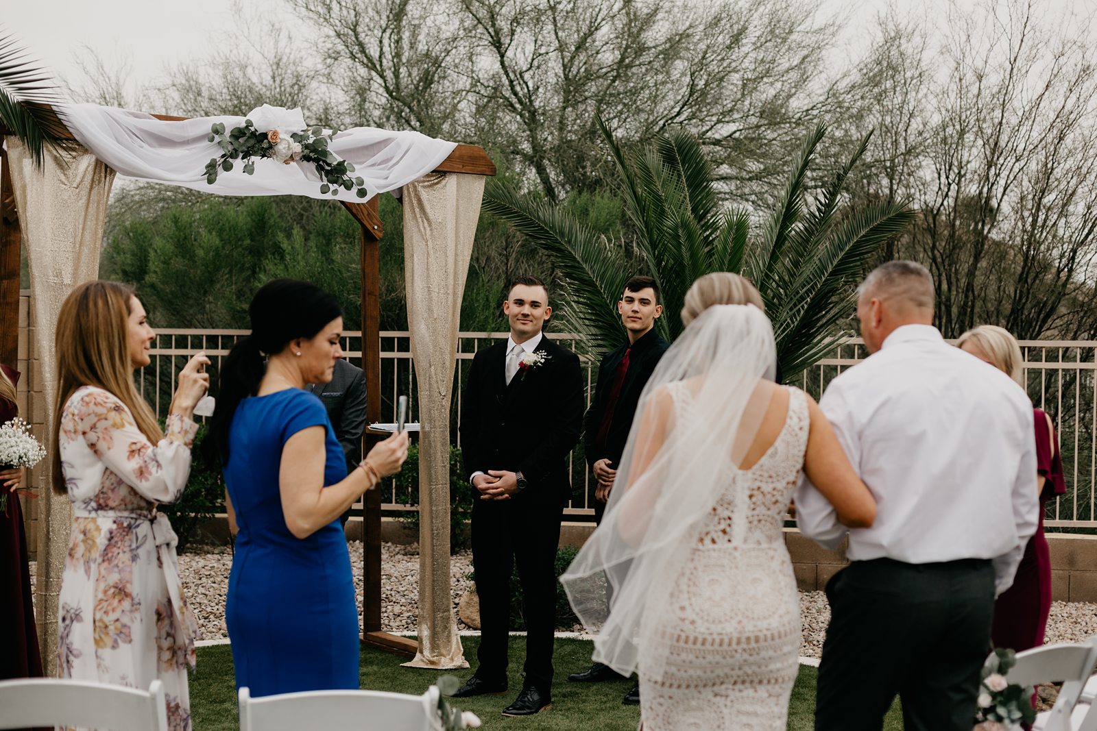 A bride walking down the aisle with her father for her intimate backyard wedding in Phoenix Arizona while the groom watches