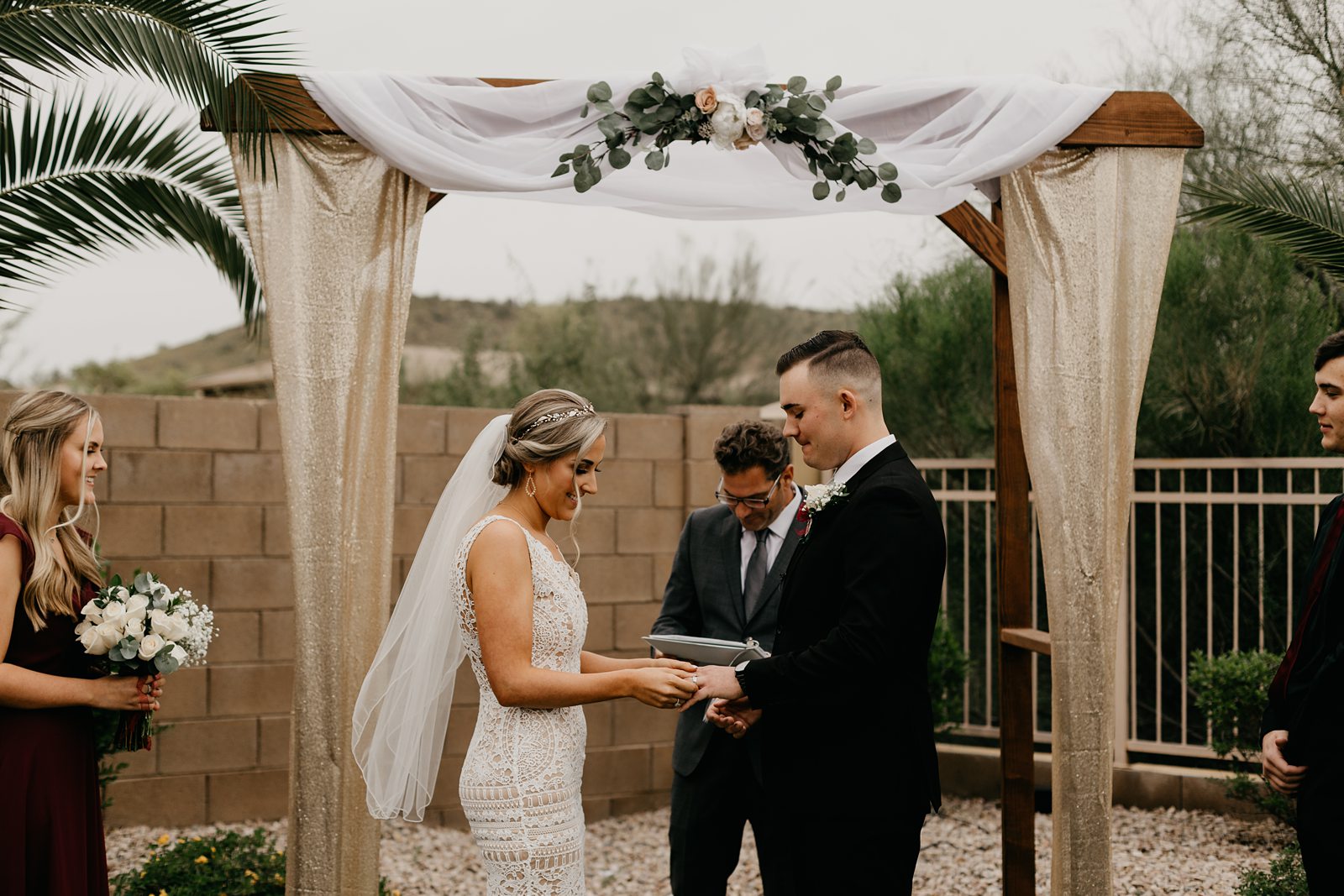 A bride and groom exchanging rings during their ceremony at their intimate backyard wedding in Phoenix Arizona on a cloudy day