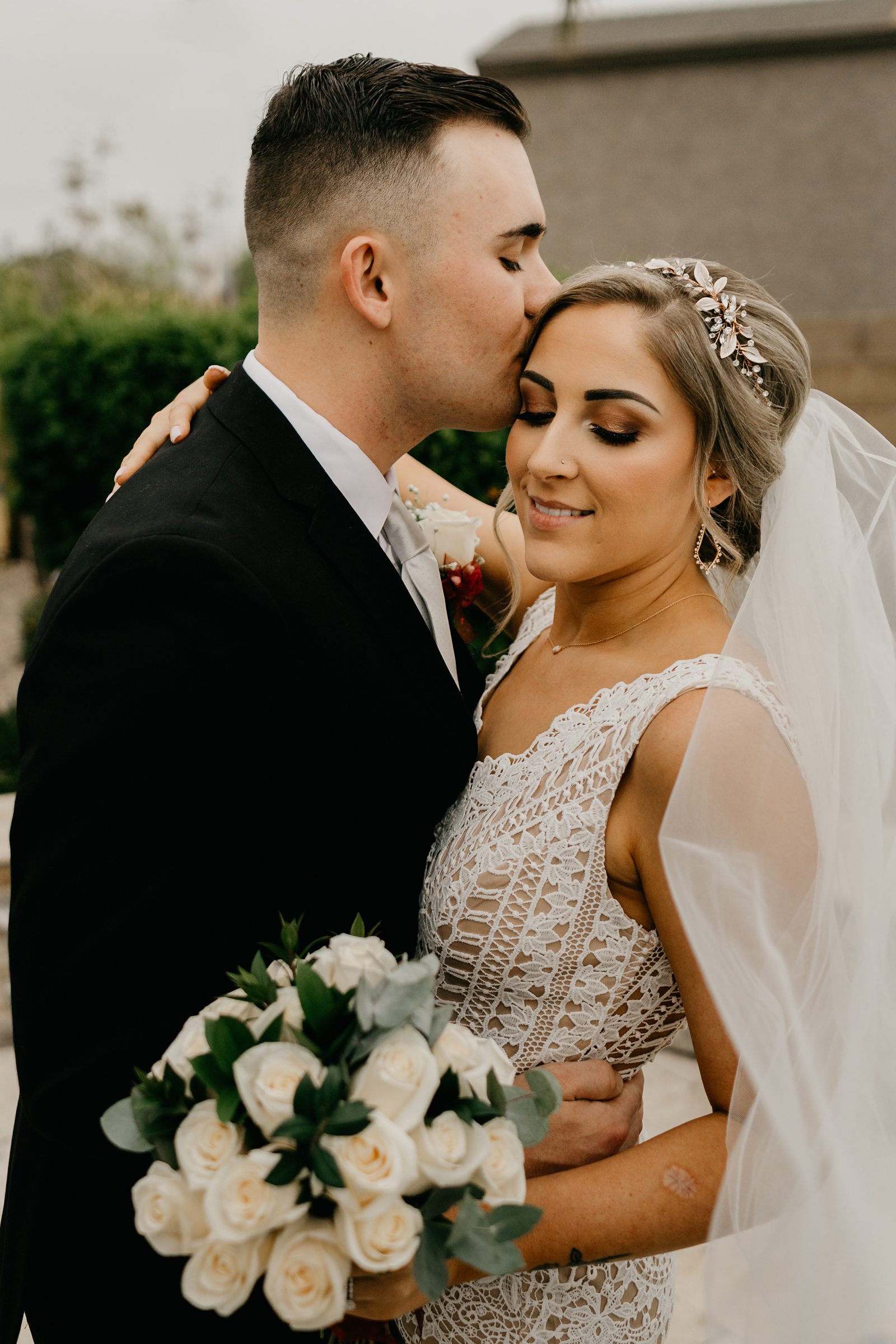 Portrait of Groom kissing his brides forehead and her smiling in their backyard wedding Glendale az