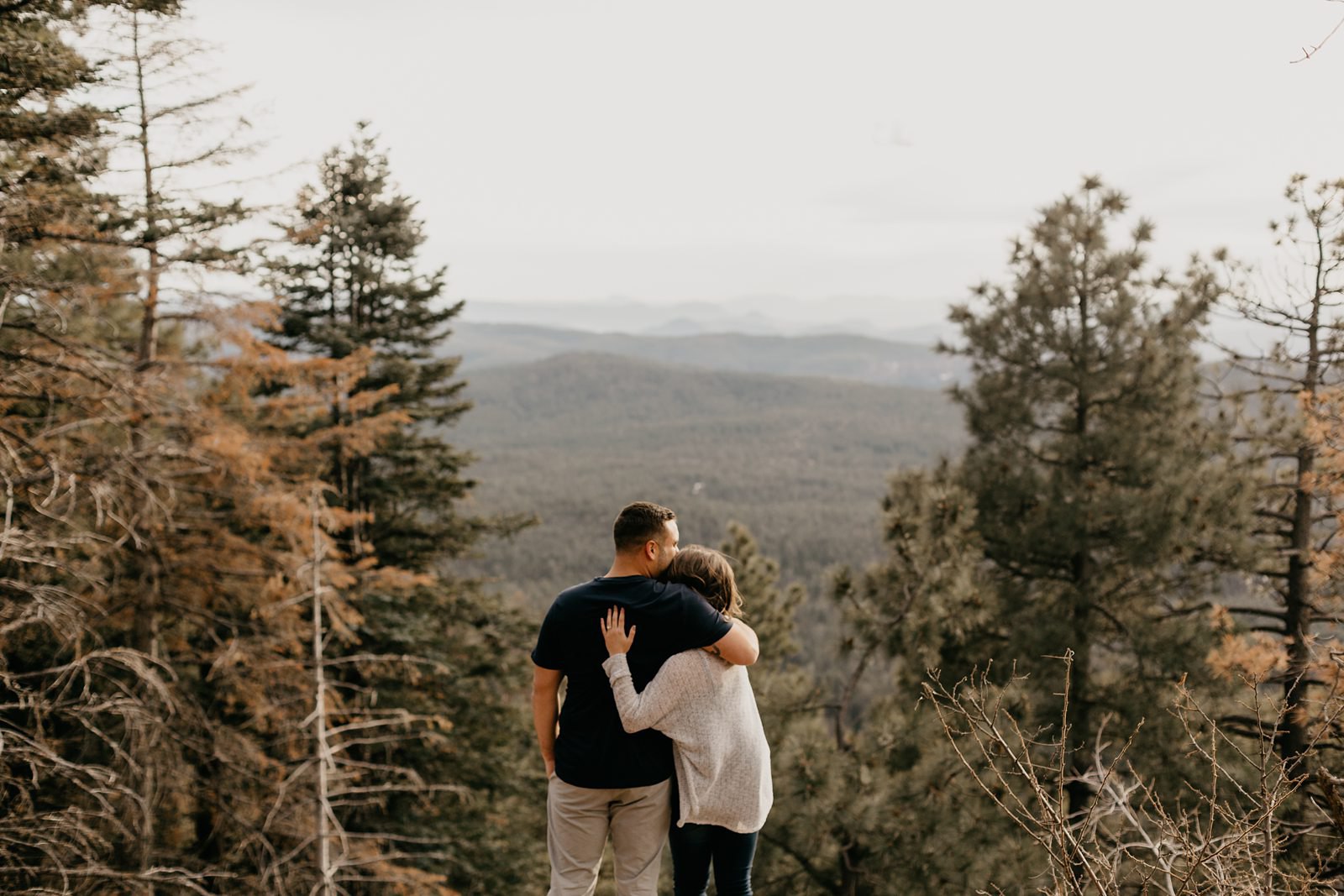 Arizona mountain top engagement couple, hugging overlooking the Mogollon rim surrounded by pine trees