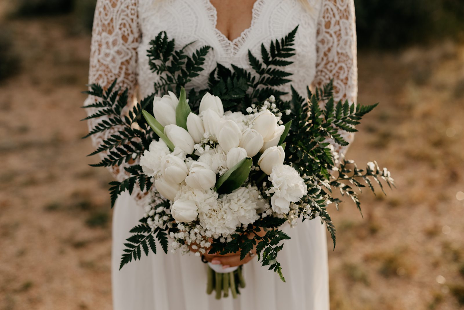 Portrait of bride in the desert of arizona in boho v neck lace dress white tulip bouquet