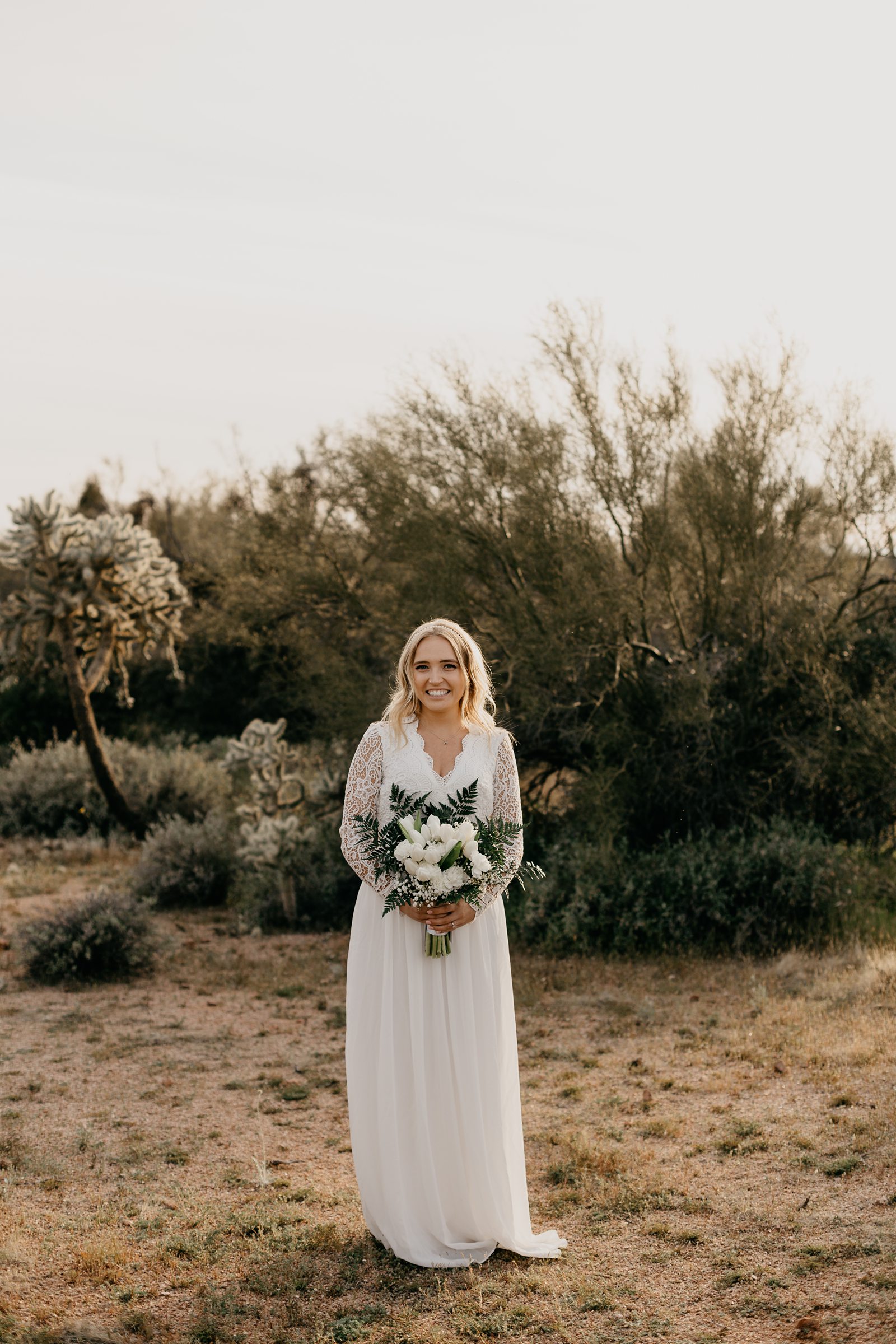 Portrait of bride in the desert of arizona in boho v neck lace dress white tulip bouquet