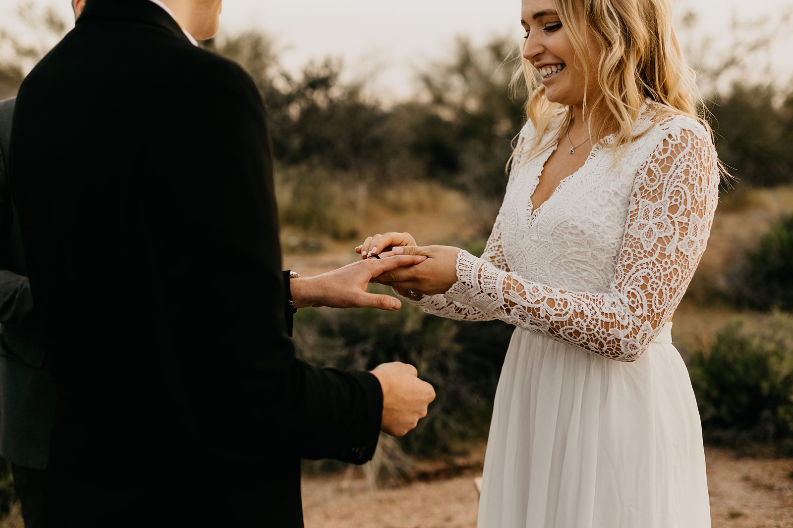 bride putting ring on groom's finger at their desert elopement in phoenix arizona wearing a boho v-neck lace dress