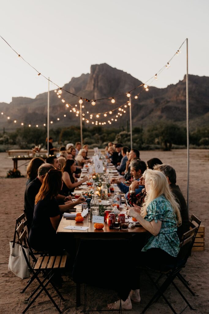 intimate wedding reception dinner in the desert, with hanging lights and mountains in the background