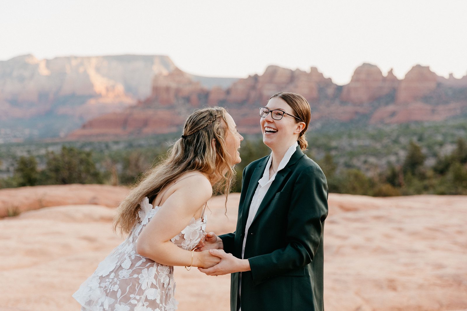 Queer sunrise red rock hiking elopement brides holding hands laughing sedona AZ