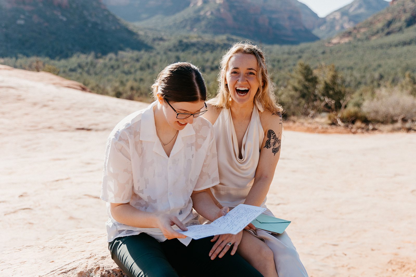 Couple laughing while reading letters, sitting on a rock