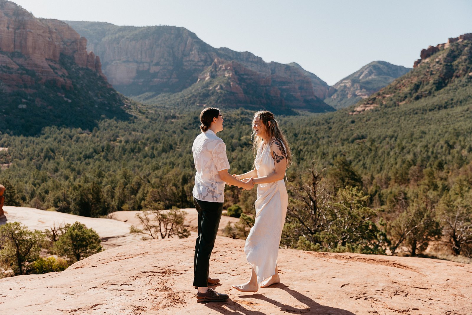 eloping couple facing each other holding hands with green sedona arizona view
