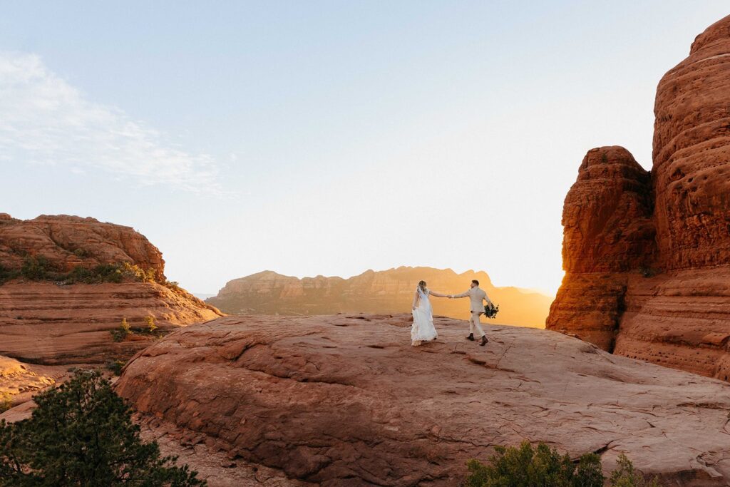 Wedding couple running across red rocks, towards the sunset