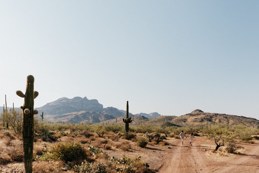 adventurous elopement couple running hand in hand down a dirt road in the desert, one of the best Arizona elopement locations