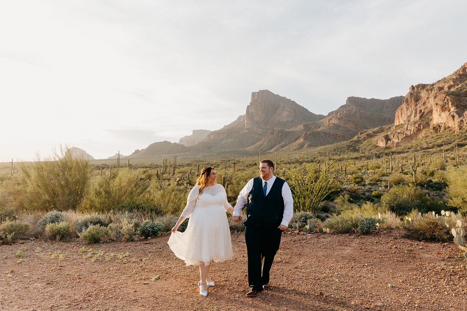 Wedding couple holding hands and walking in the Arizona desert with the Superstition Mountains in the background, at one of the best Arizona elopement locations