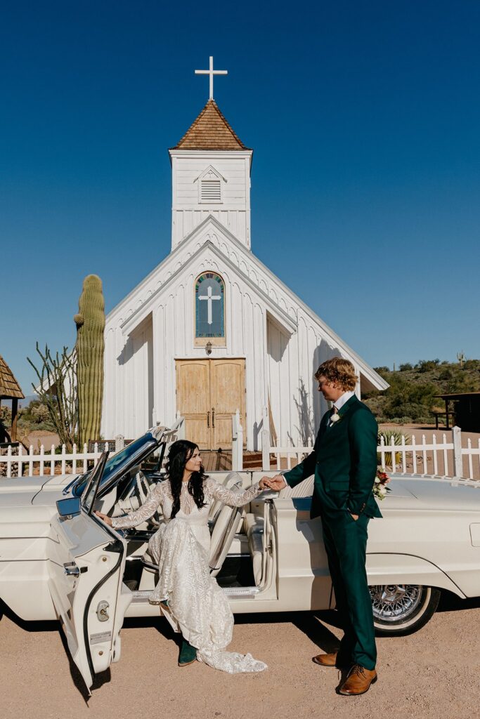 Eloping couple getting out of a vintage white convertable in front of a white Elvis chapel in the arizona desert