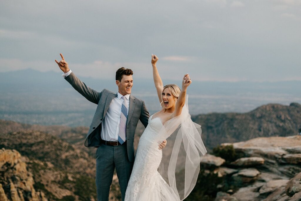 an eloping couple with their arms in the air cheering, on top of Mount Lemmon in Tucson AZ